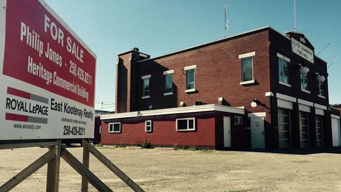 Picture of the former fire hall in Cranbrook, with a 'for sale' sign in the foreground. 
