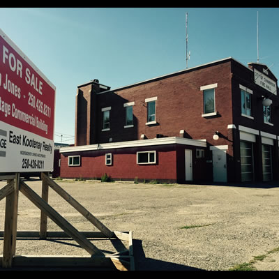 Picture of the former fire hall in Cranbrook, with a 'for sale' sign in the foreground. 