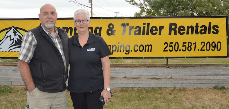 Christie and Menno Dueck standing in front of their Fisher Peak Camping & Trailer Rentals sign. 