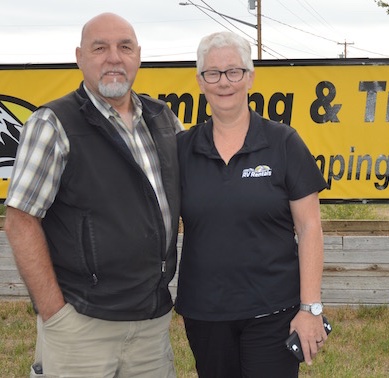 Christie and Menno Dueck standing in front of their Fisher Peak Camping & Trailer Rentals sign. 