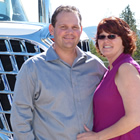 Photo of a man in a blue shirt and a woman in a pink shirt standing together in front of a semi truck. 