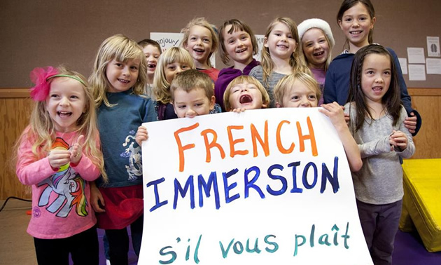 Picture of group of young students holding a sign that says, 'French Immersion - s'il vous plait'