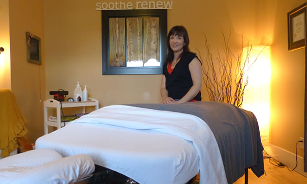 A woman with dark hair sitting at the end of a massage table. 