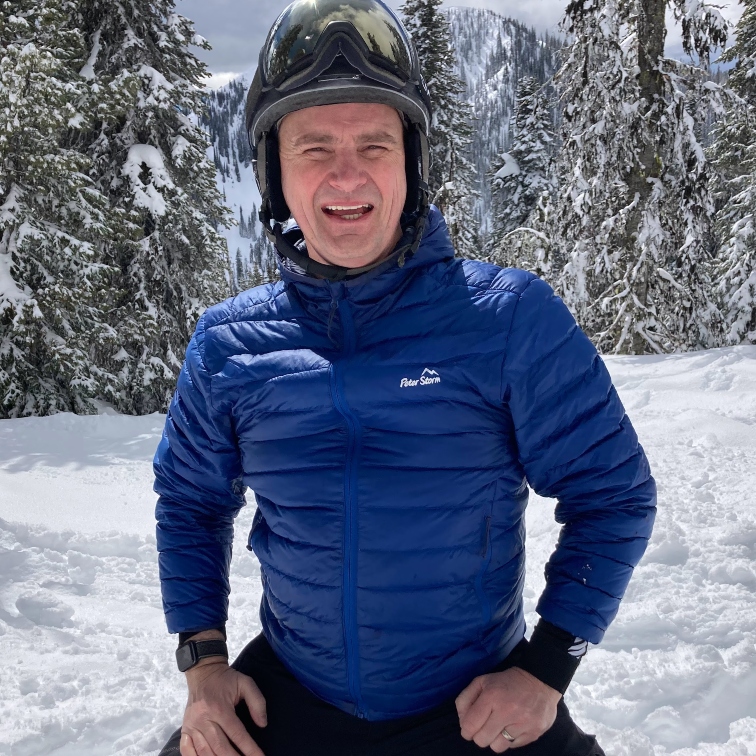 Derek in blue winter gear kneeling in the snow smiling