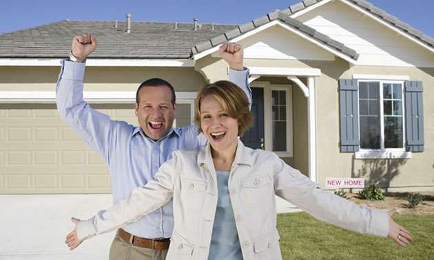 Couple with arms raised in front of a new home.