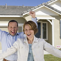 Couple with arms raised in front of a new home.