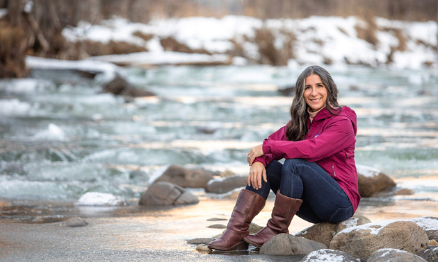 Jennifer King wearing a pink jacket and sitting beside a rushing river