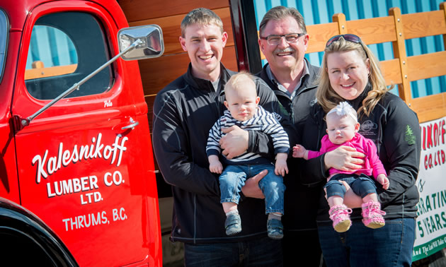 A father, his daughter, son and grandchildren standing by a red truck. 