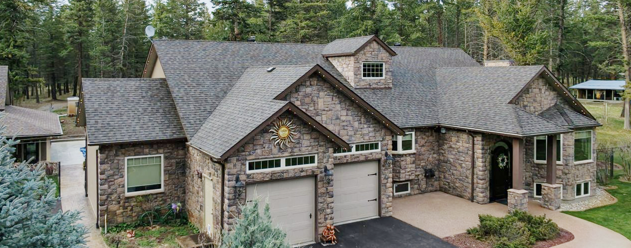 Exterior drone shot of a house with double garage and stonework, and a grey asphalt shingle roof
