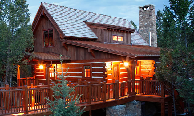 Log cabin-type house, lit up at dusk. 