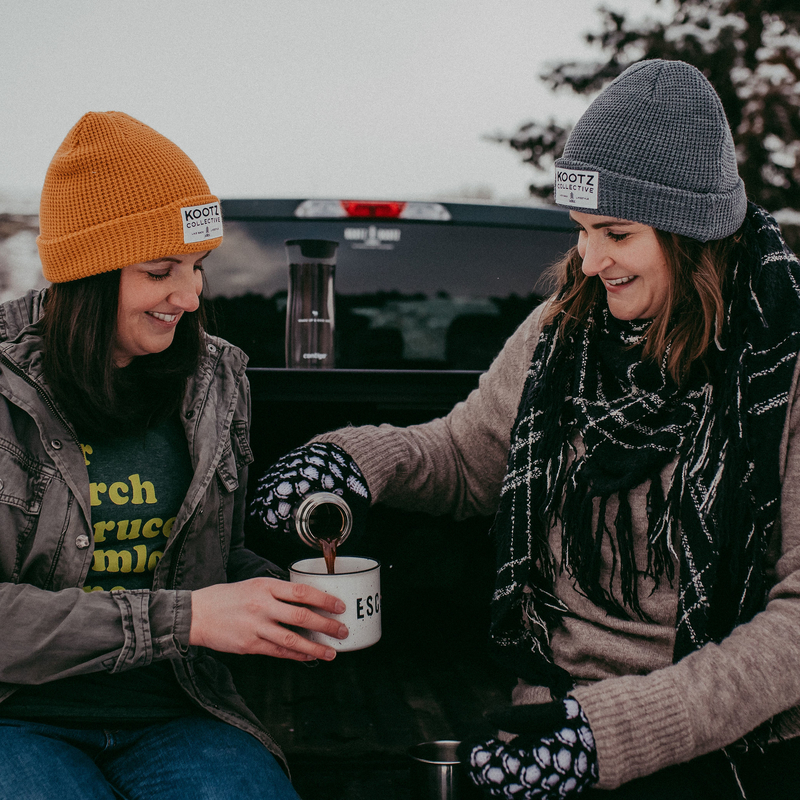 Kelsey Gosse (Left) and Leah Pavlick (right) wearing Kootz Collective merchandise and pouring coffee into a mug 