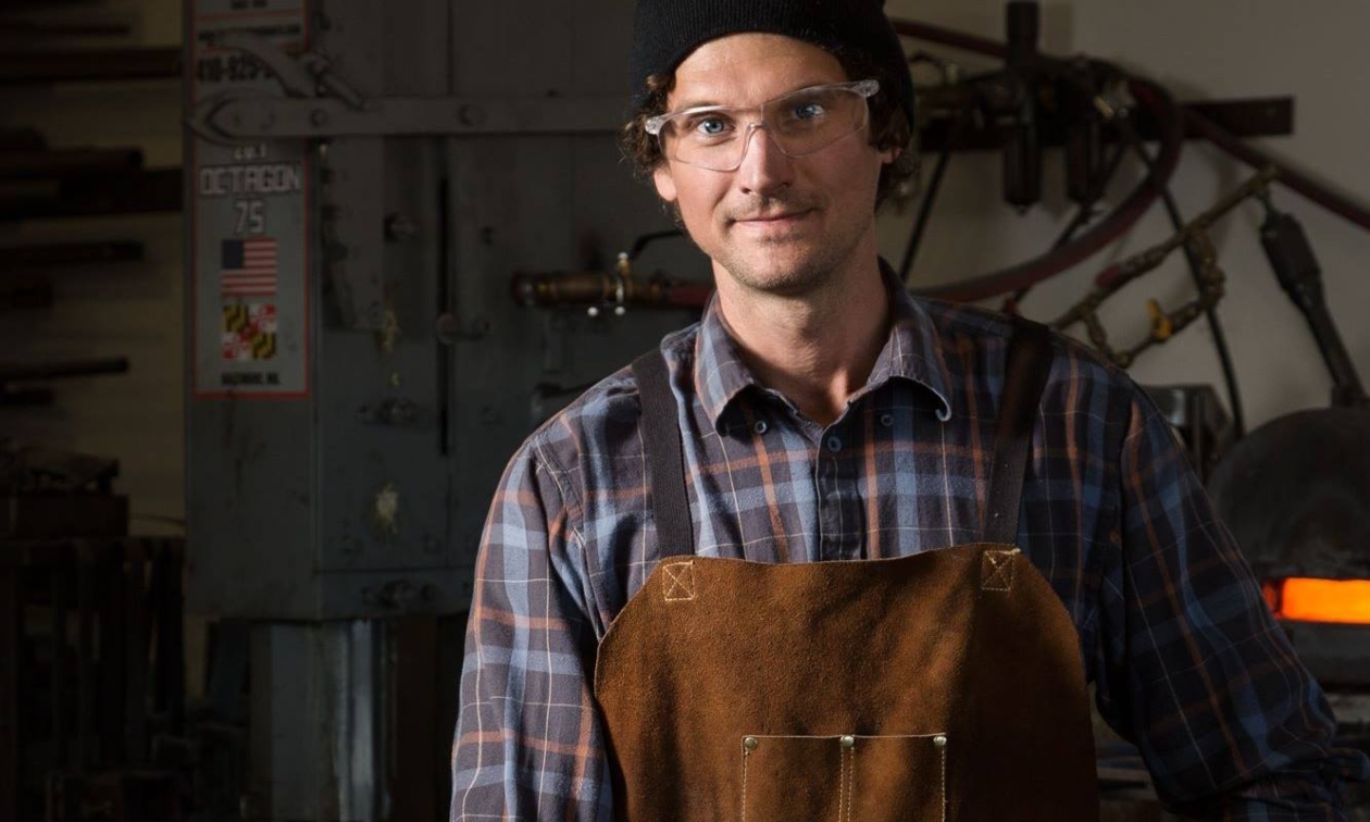 Kyle Thornley wearing his blacksmithing apron and smiling at the camera