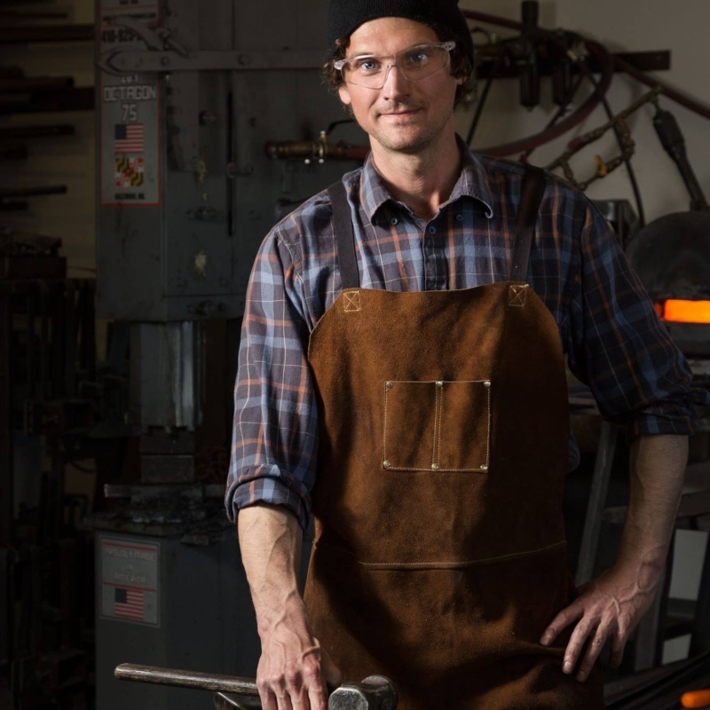 Kyle Thornley wearing his blacksmithing apron and smiling at the camera