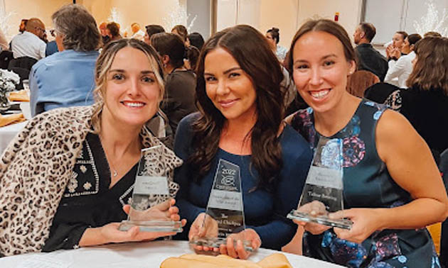 Female owners of Moonrise Boutique, The Roasted Chickpea and Tailout Brewing, sitting at table with awards and smiling into camera. 