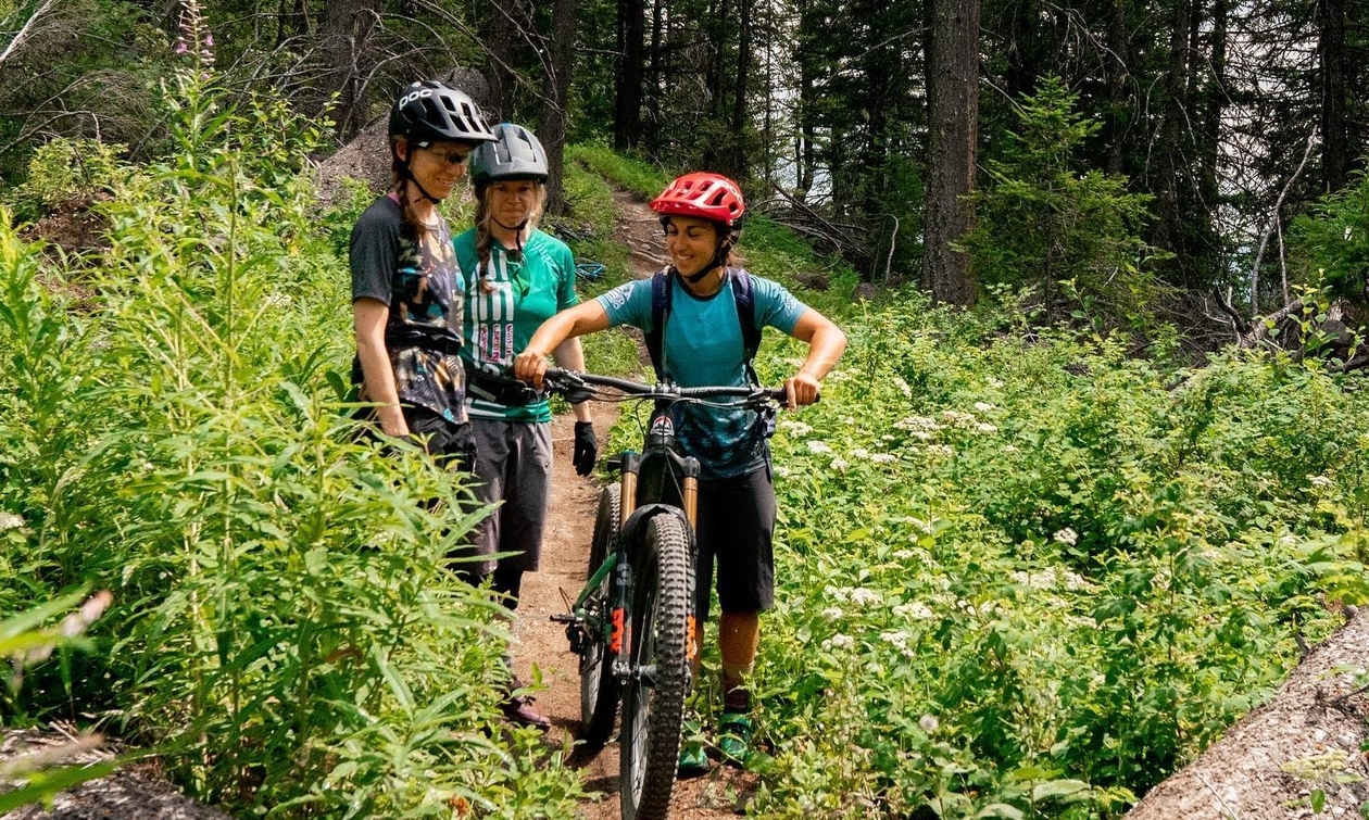 Audrey Duval in foreground, standing with two other woman, all have mountain bikes. 