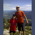 A man and young boy stand together on top of a mountain in summer