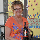 Donna Alexander sitting on a patio chair with a bottle of her award winning wine in Golden, BC