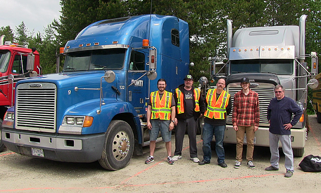 A group of trucking students standing between two big semi-trucks. 