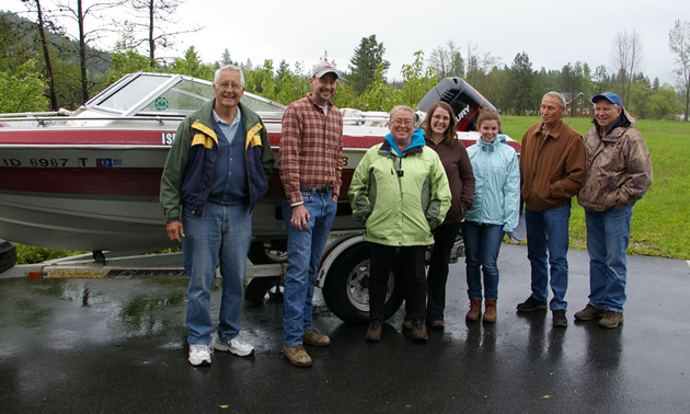 A group stands in front of a red motor boat.