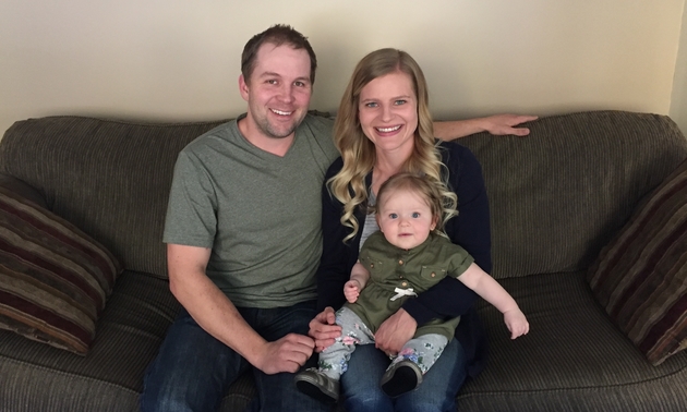 Derek Curlew sitting on a sofa with his wife and their new baby