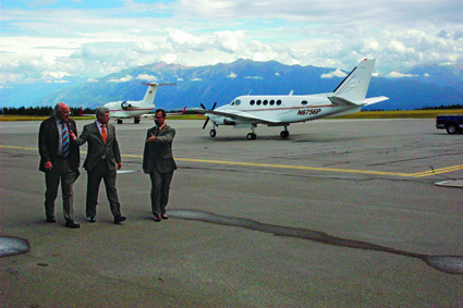 Three men in suits walk across the tarmac with two planes behind.