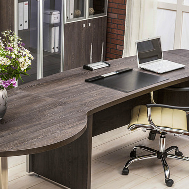A modern office with only a laptop computer and flowers on top of the desk. 