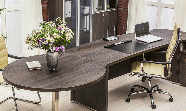 A modern office with only a laptop computer and flowers on top of the desk. 