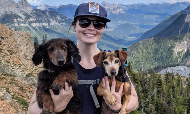 Steph McGregor holding two dogs and standing on a hiking trail