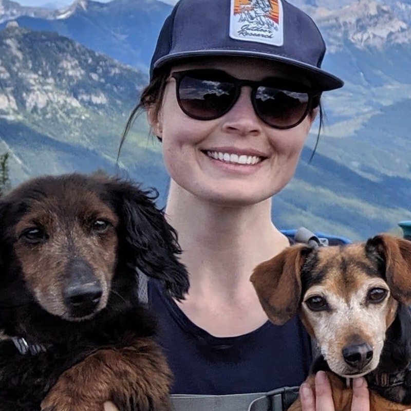 Steph McGregor holding two dogs and standing on a hiking trail