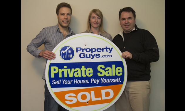 two men and a woman hold up a large round sign for PropertyGuys.com that says Private Sale: Sold