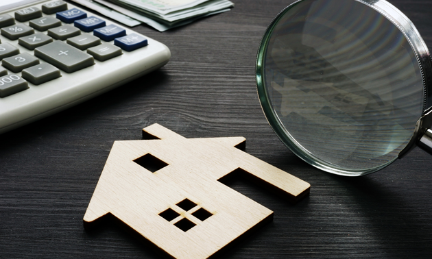 Close up of flat wooden house shape, magnifying glass and computer keyboard. 