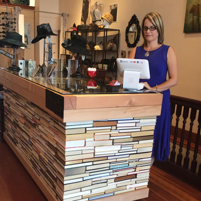 Owner Zabrina Nelson of Revival Boutique stands behind a desk made of over 1,000 recycled books glued together.