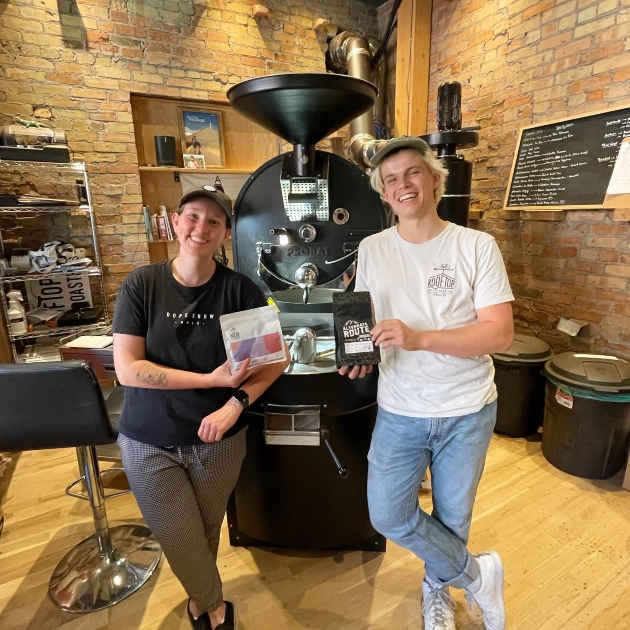 Owners of Rooftop Coffee Roasters next to a roaster, holding beans