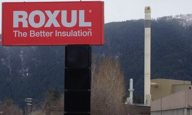 A red sign in front of a smoke stack reads 