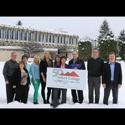 Members of the Selkirk College 50th Anniversary Committee stand in front of the Castlegar Campus with a new logo that recognizes five decades of post-secondary in the West Kootenay-Boundary. 