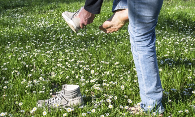A man is taking off his runners to stand in a lawn of grass and white flowers.