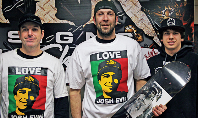 A man holding a skateboard with his brother's picture on it.