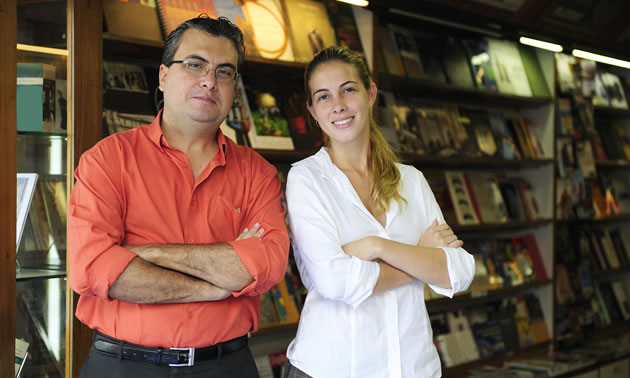 A man and a woman stand in front of shelves of books.
