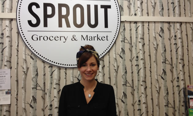 Chantel Delaney is standing in front of the Sprout Grocery sign with birch tree wallpaper on the wall.