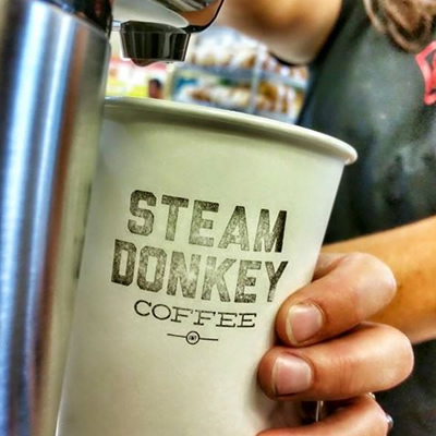 Picture of a person holding a coffee cup with the words 'Steam Donkey Coffee' printed on it. 