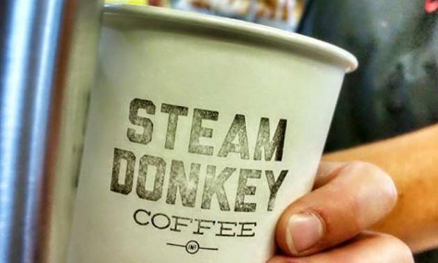 Picture of a person holding a coffee cup with the words 'Steam Donkey Coffee' printed on it. 