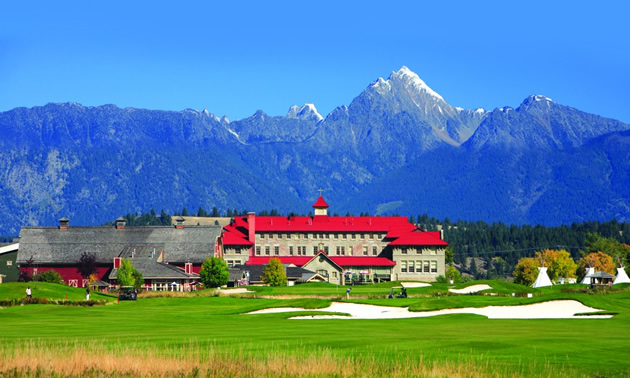 View of golf course with mountains and St. Eugene building in the far distance—building has red roof.