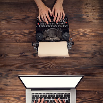 Picture of person using typewriter at top of picture, with laptop user below. 