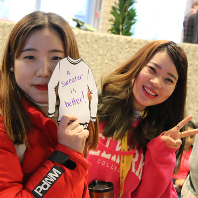 Two female students are wearing warm layers of clothes and are holding a sign that says 