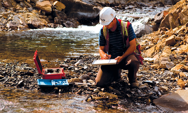 Teck worker kneeling in a creek taking samples