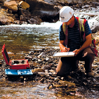 Teck worker kneeling in a creek taking samples