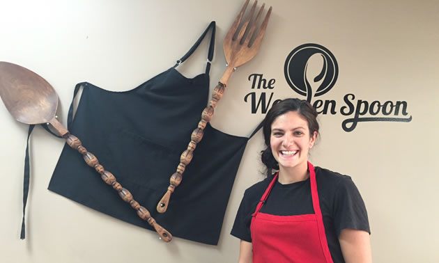 Owner and chef Kayla Sebastian of The Wooden Spoon Bistro & Bake Shop in Grand Forks is standing in front of the bistro's logo.