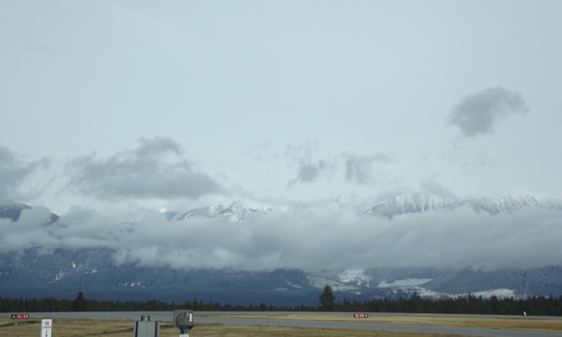 an airstrip as viewed from inside the terminal building with mountains in the distance