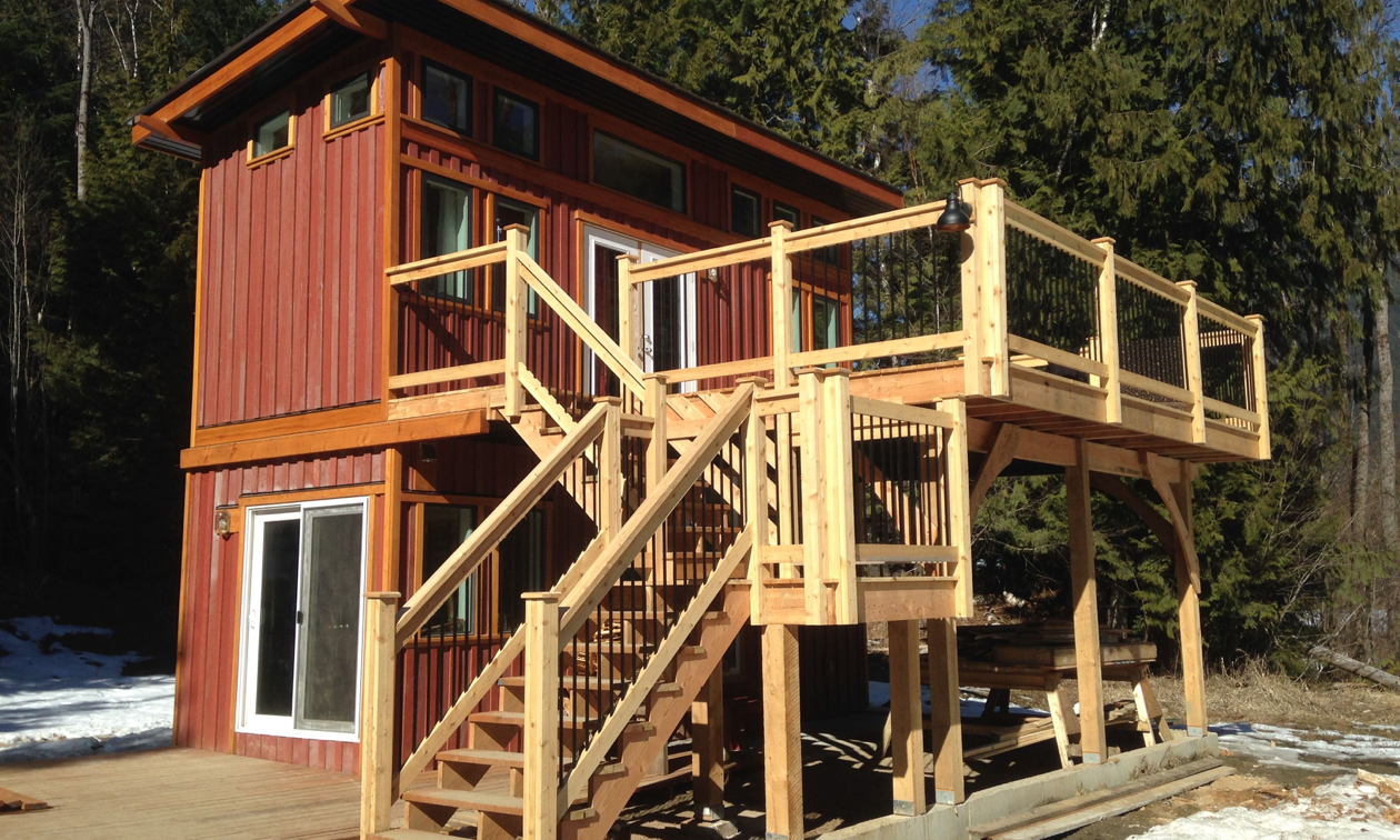 A tiny two-storey house has outside stairs leading to an open deck on the second level.