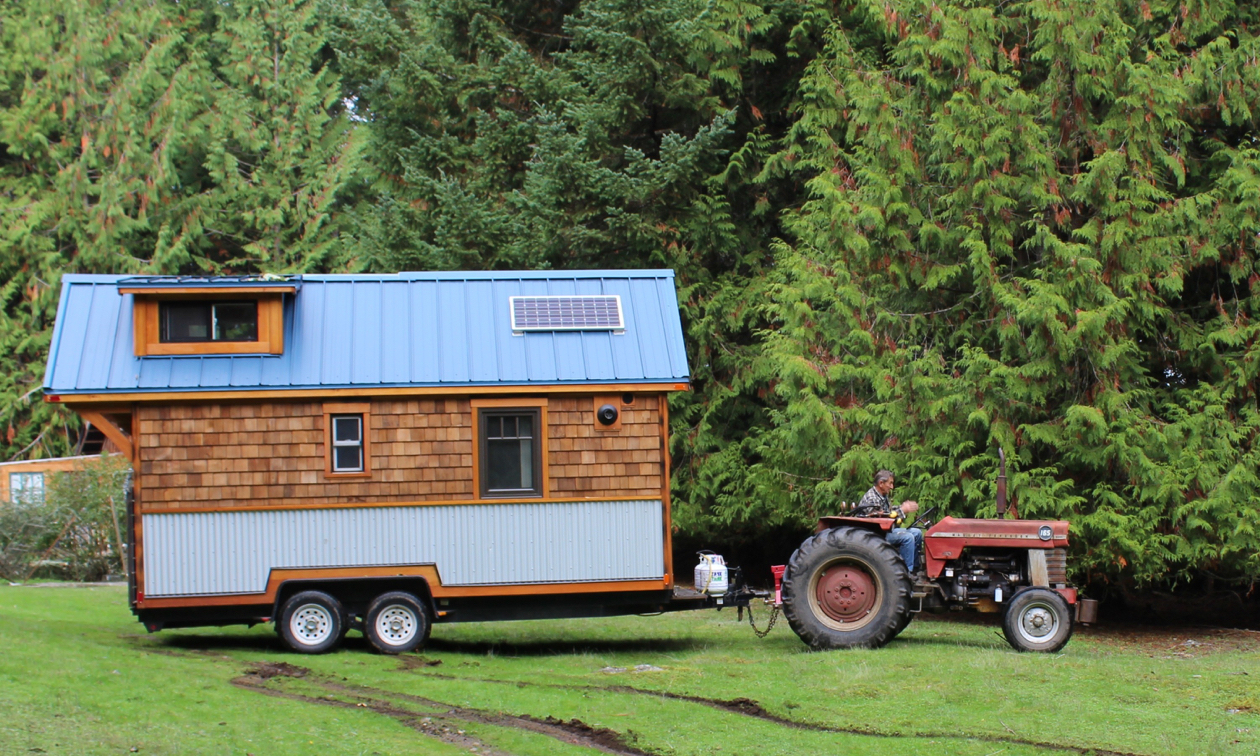 A tiny house is being pulled by a tractor.